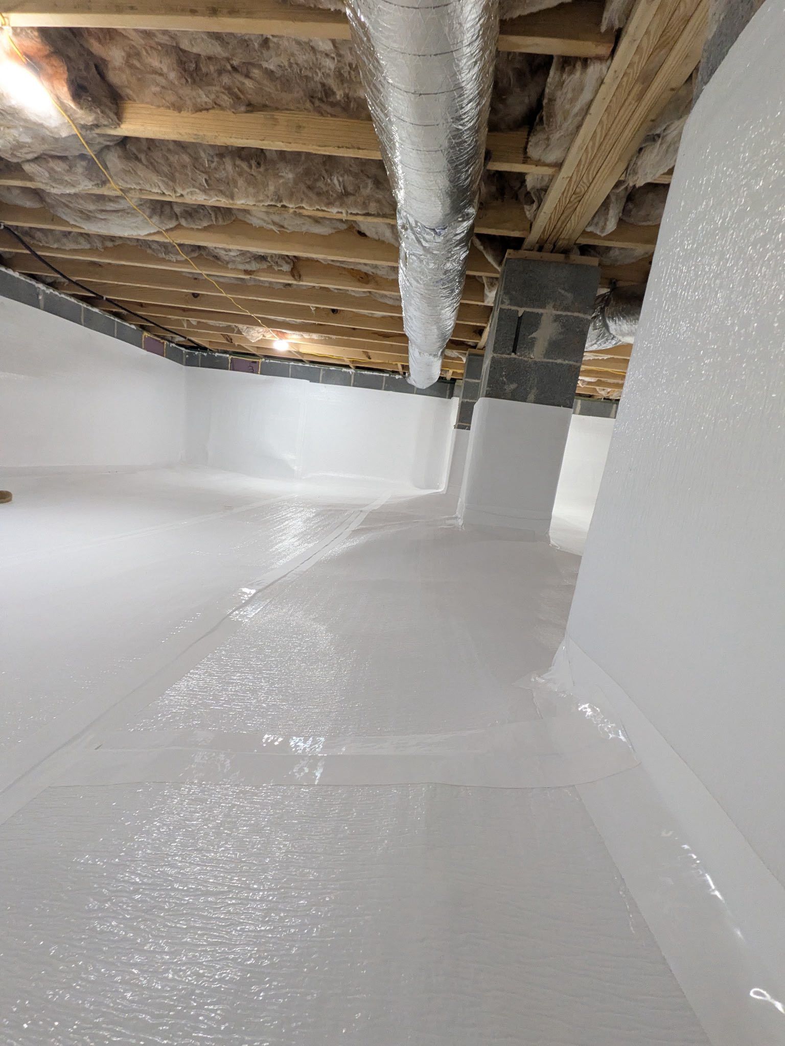 A clean, empty basement with white walls, a polished white floor, and exposed wooden ceiling beams with silver ductwork.