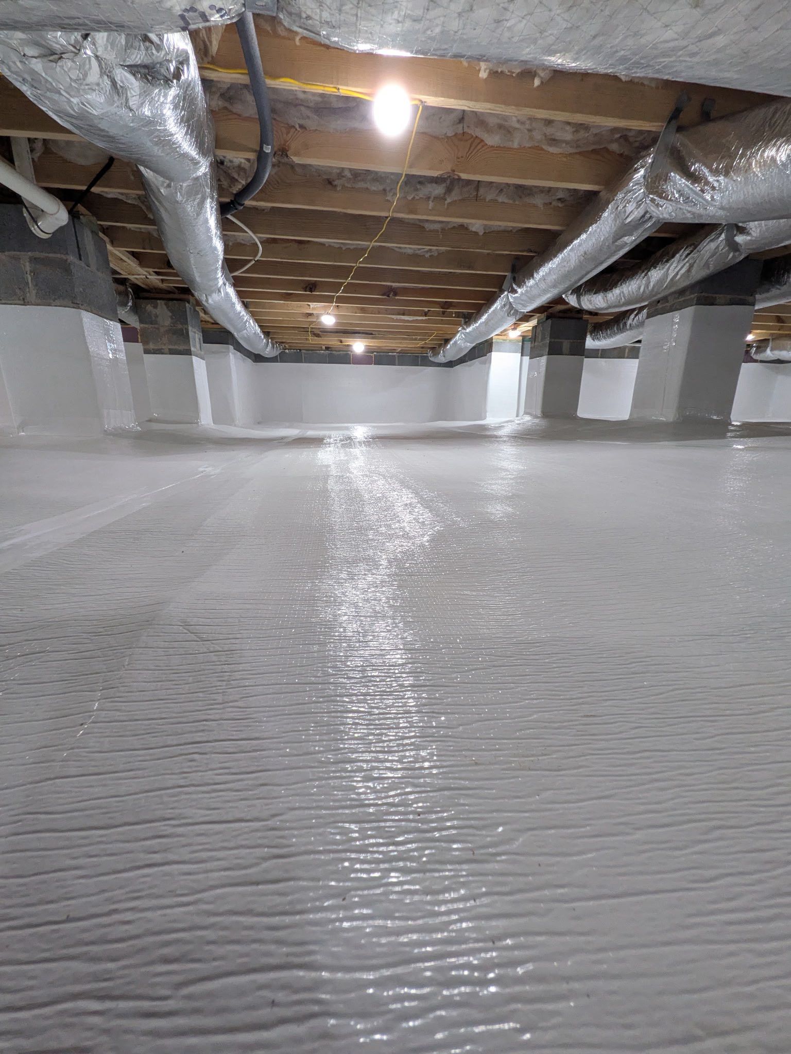 A clean, encapsulated crawl space with a white vapor barrier covering the floor and concrete piers under floor joists.