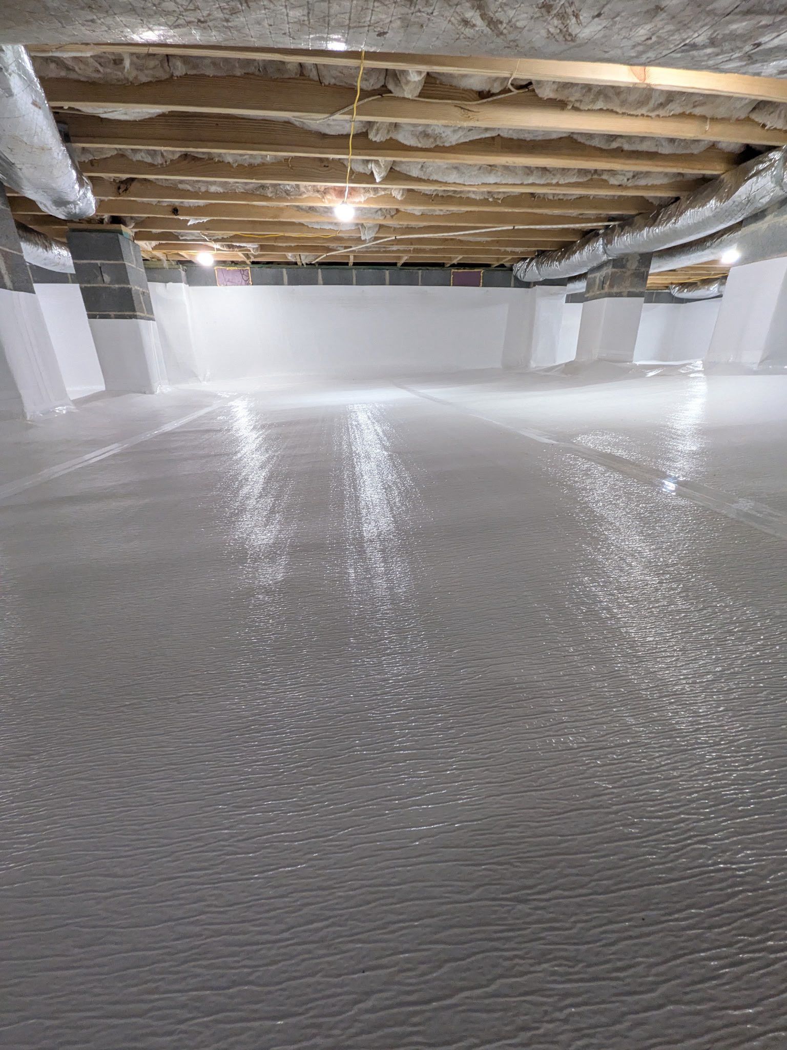 A newly poured, glossy gray concrete floor in a basement with exposed wooden ceiling joists and white walls.