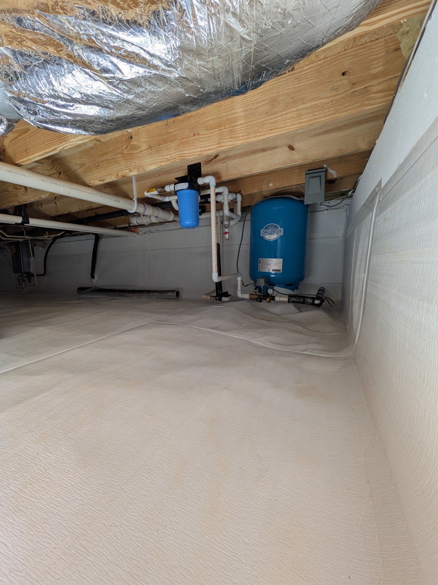 A blue water pressure tank and a small water filter mounted to floor joists in a clean, encapsulated crawlspace.