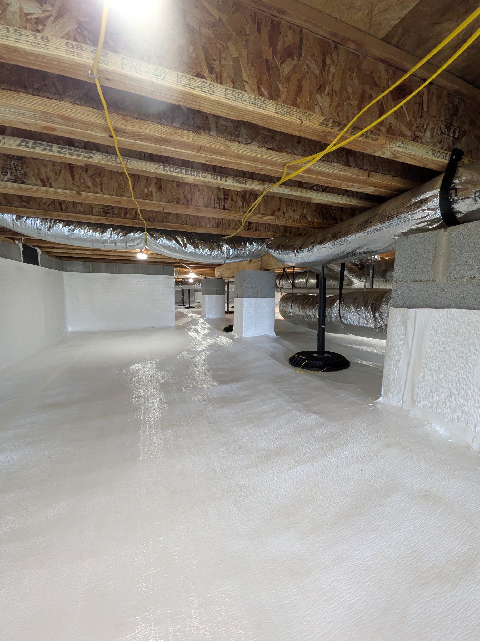 A clean, encapsulated crawl space with white-coated walls and flooring, exposed wooden joists, and insulated HVAC ducts.