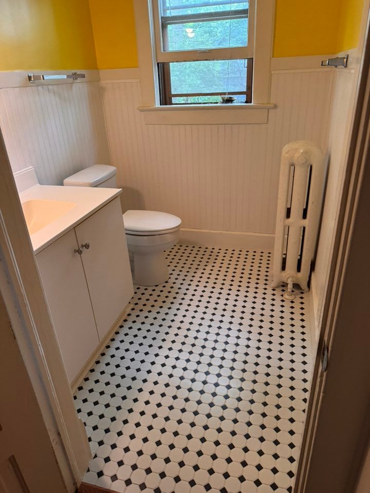 A small bathroom with white beadboard walls, bright yellow upper walls, a vanity, toilet, and black-and-white tile floor.