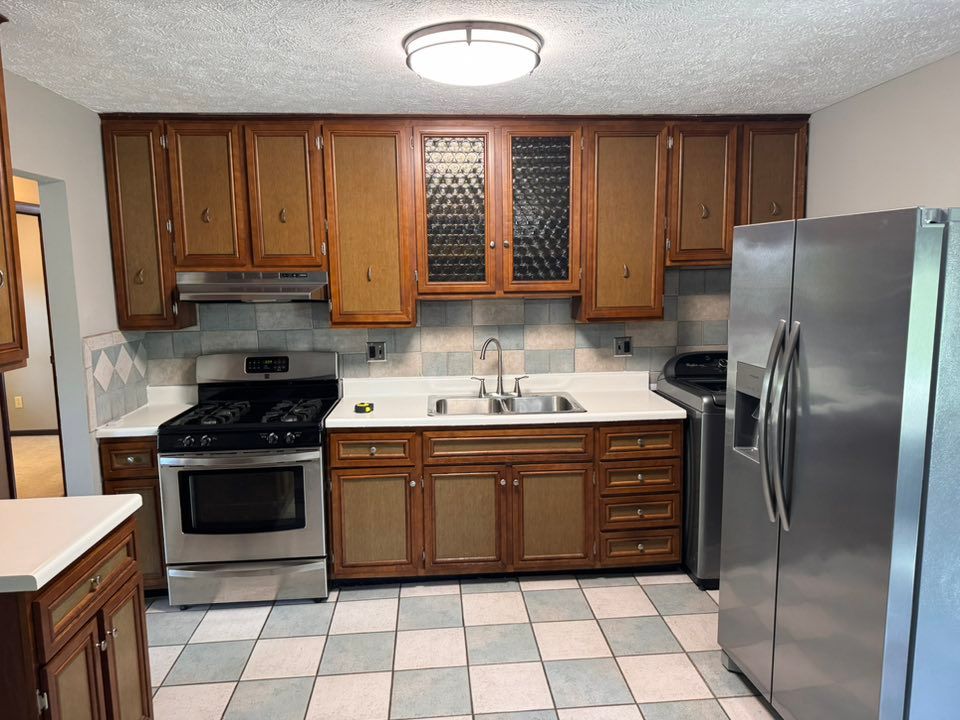 A kitchen with wood cabinets, stainless steel appliances, a double sink, and a checkered tiled floor under a flush light.