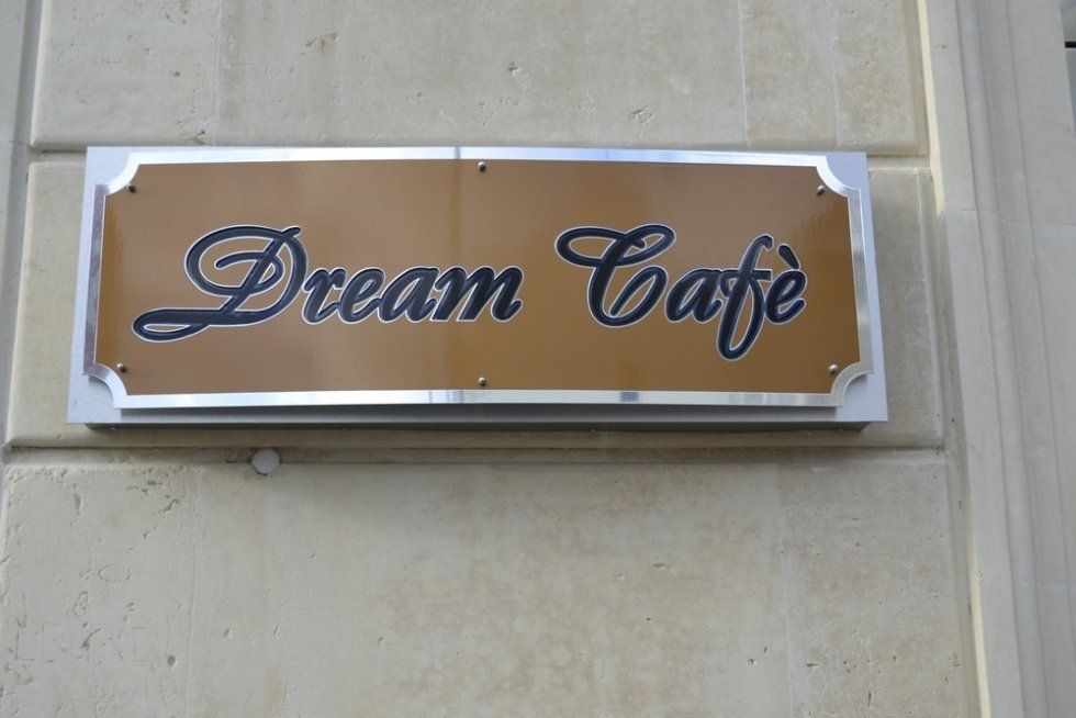 Insegna del Dream Café, sfondo marrone, finiture argentate, su una parete beige.