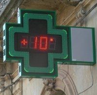 Cartello verde a forma di croce della farmacia che indica una temperatura di 10 gradi.