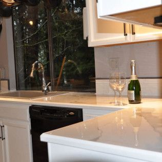 Modern kitchen with white countertops, black dishwasher, sink by window, and a champagne bottle with glasses