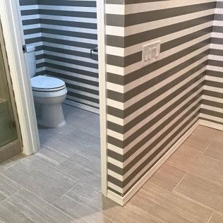 Bathroom with gray-and-white striped walls, tiled floor, and a toilet visible through an open doorway