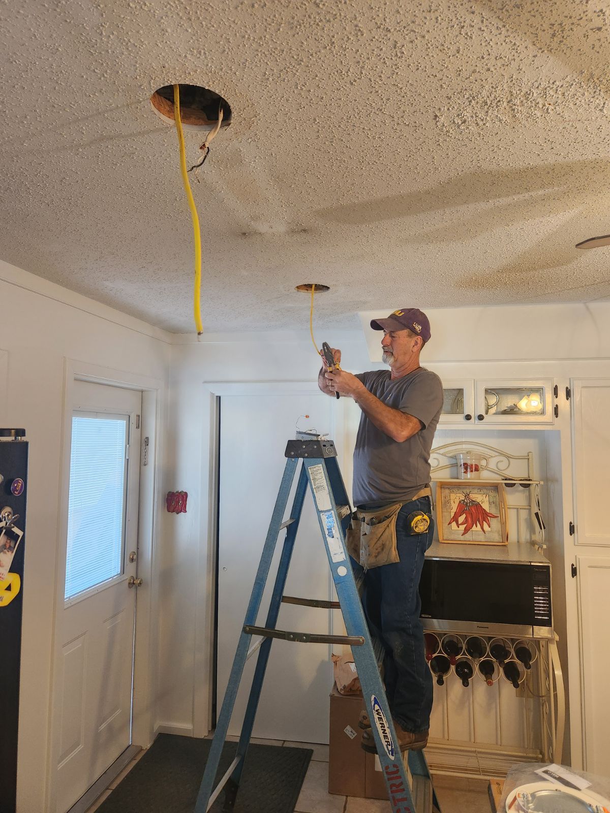 A man is standing on a ladder in a kitchen fixing a light fixture.