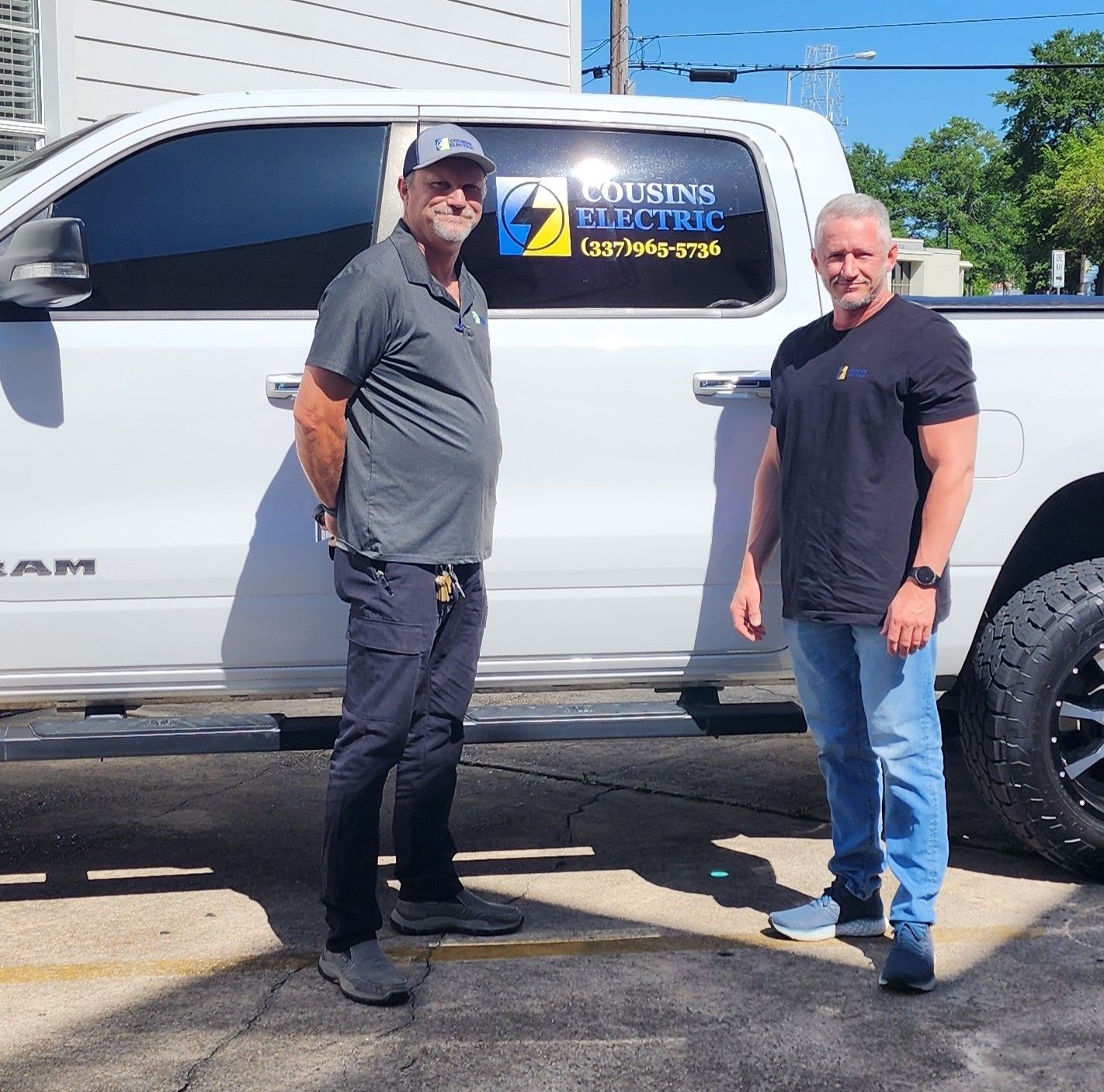 Two men are standing in front of a truck that says cousins electric