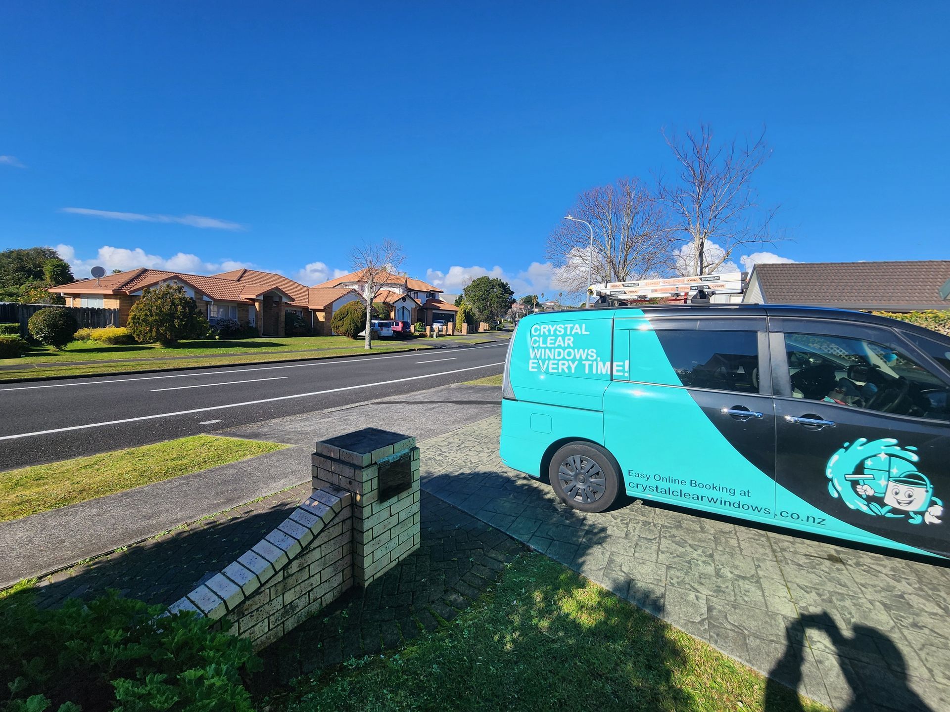 Turquoise service van parked by a suburban street under a bright blue sky