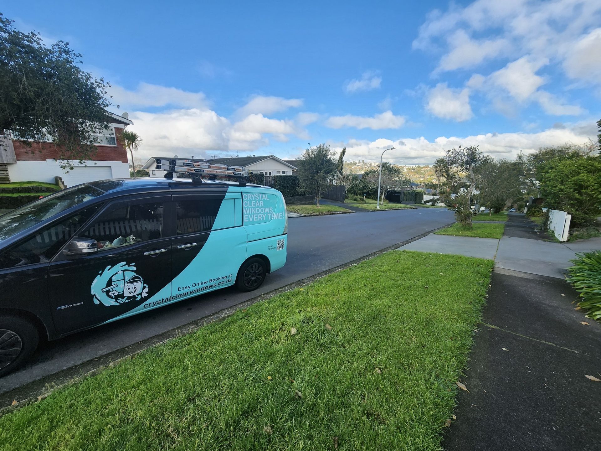 Turquoise van parked on a residential street beside a grassy verge under a partly cloudy sky