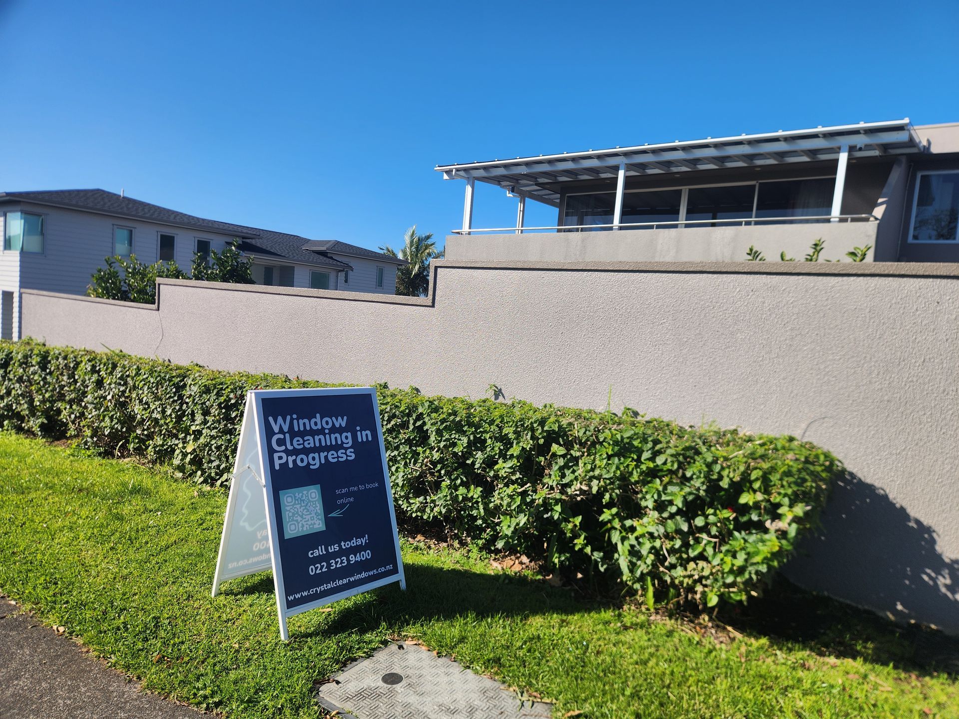 Blue sign on a lawn in front of hedges and a beige building under a clear sky.