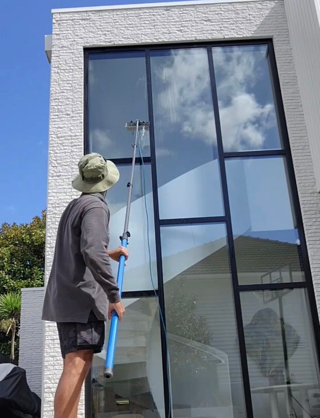 Person using a long-handled window cleaner on a large modern house window