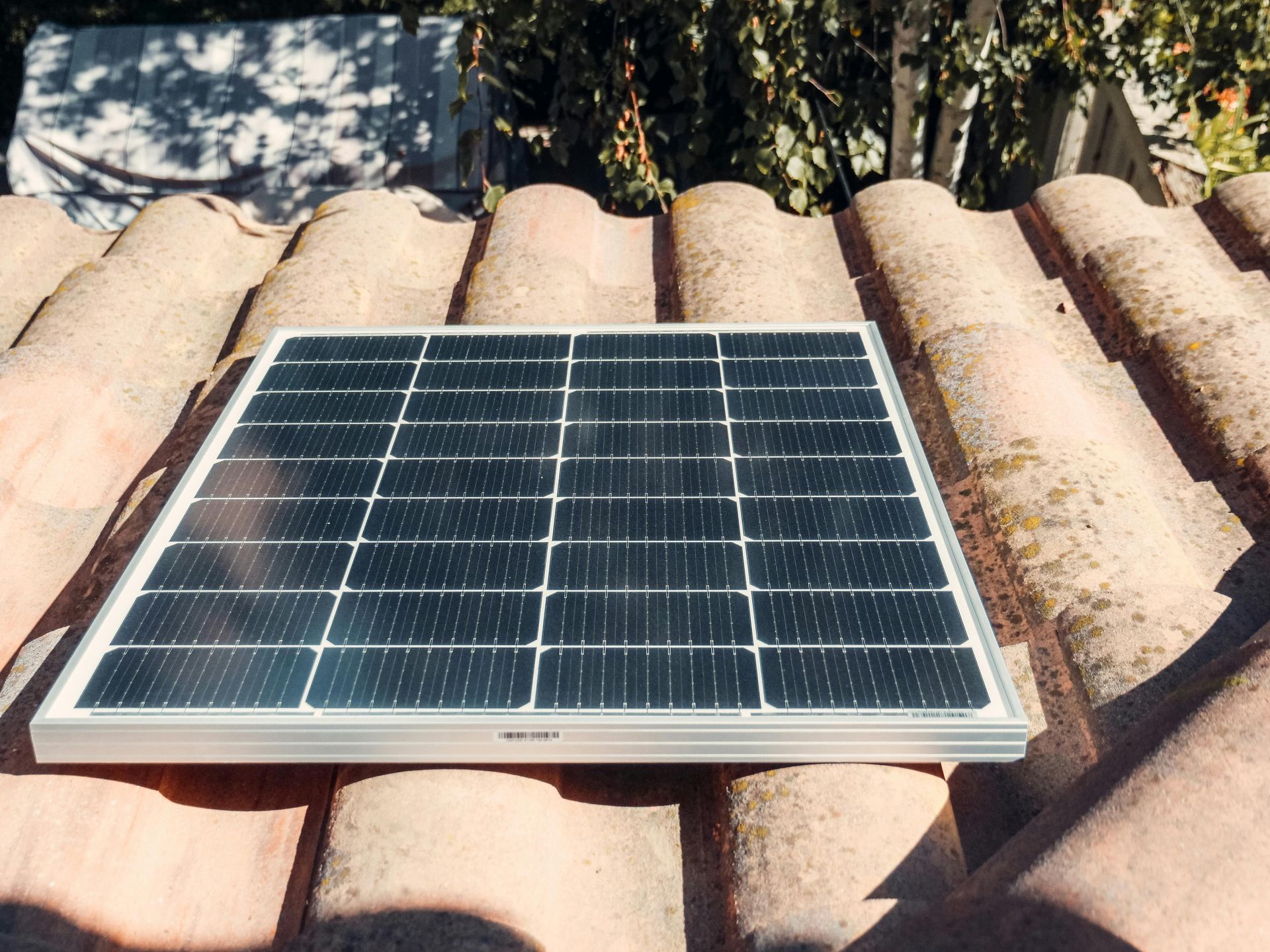 Solar panel on a weathered terracotta tiled roof, outdoors in sunlight.
