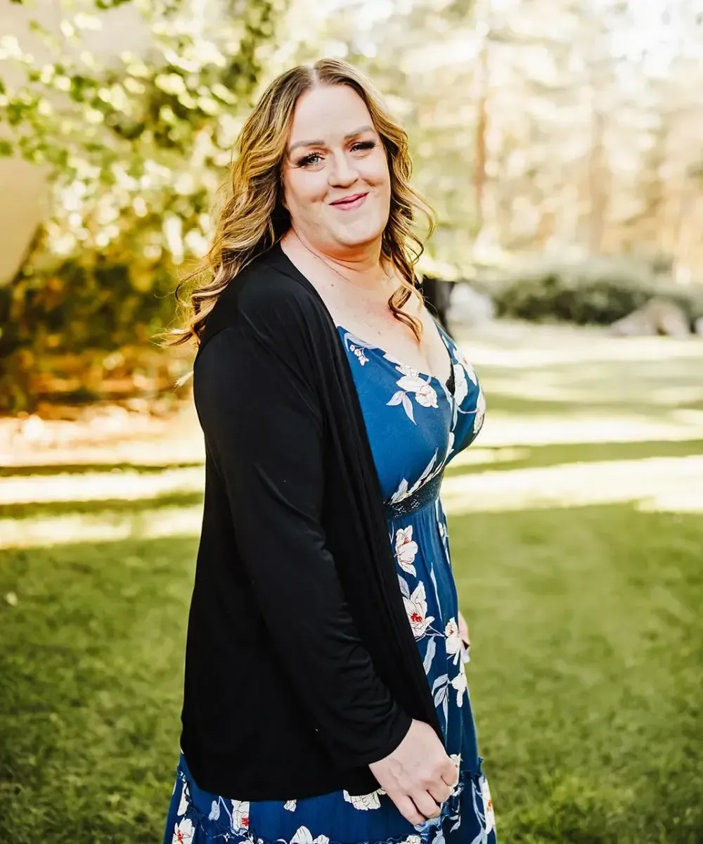 A woman in a blue dress and black cardigan is standing in the grass.