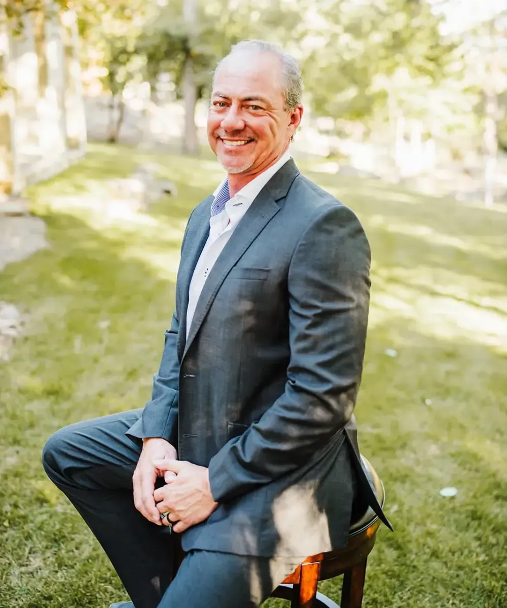 A man in a suit is sitting on a stool in the grass.