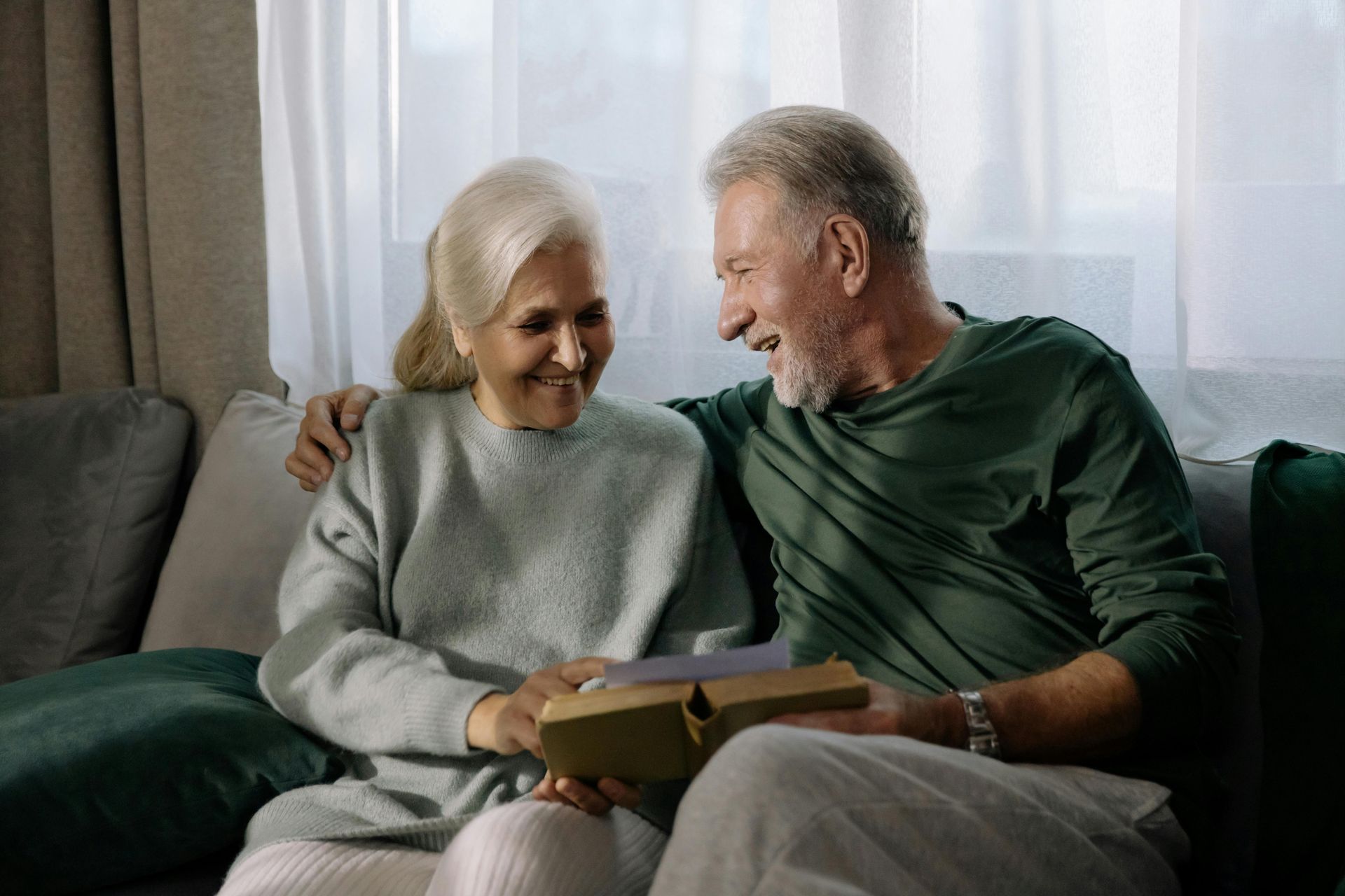 An elderly couple is sitting on a swing in front of a house.