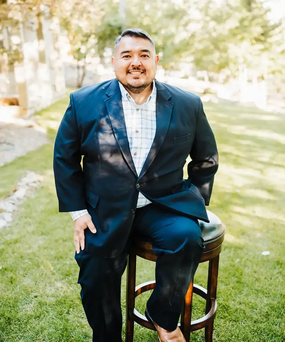 A man in a suit is sitting on a bar stool in the grass.