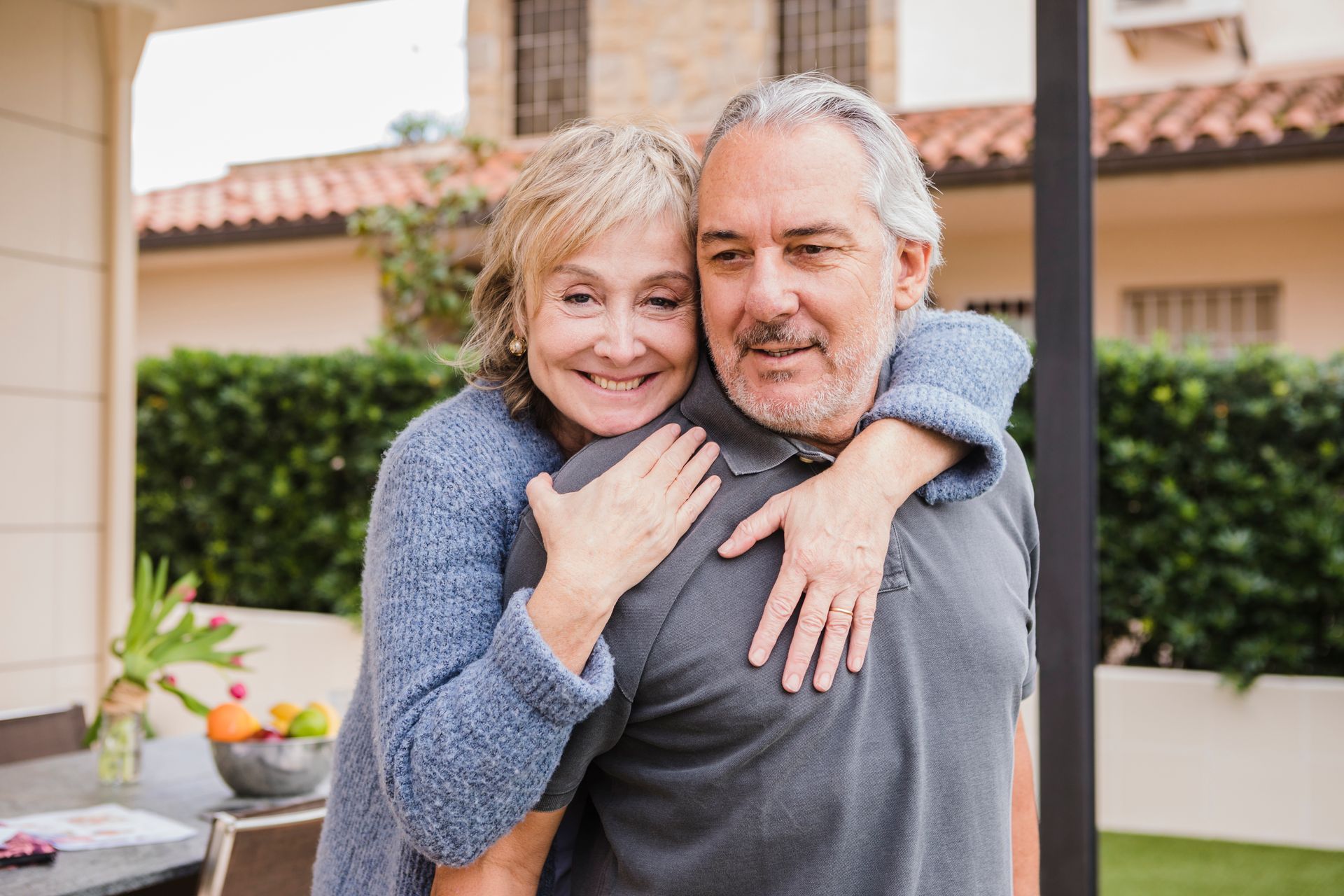 An elderly couple is sitting on a swing in front of a house.