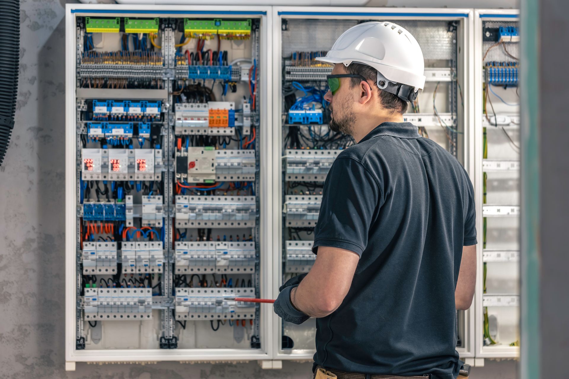 Technician inspecting an electrical control panel with wiring and circuit breakers in a metal cabinet