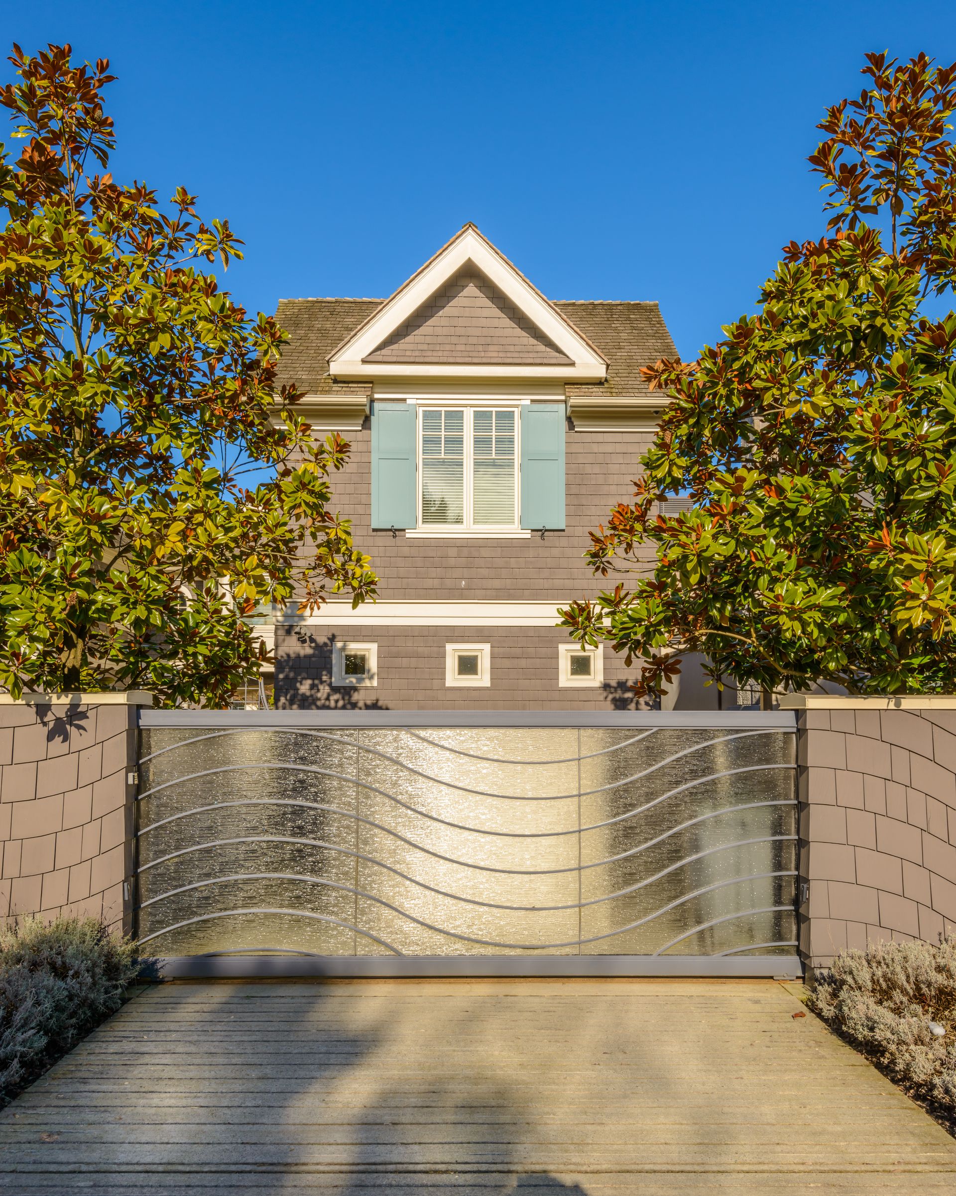 Modern house with a silver metal gate, brick walls, and trees under a blue sky