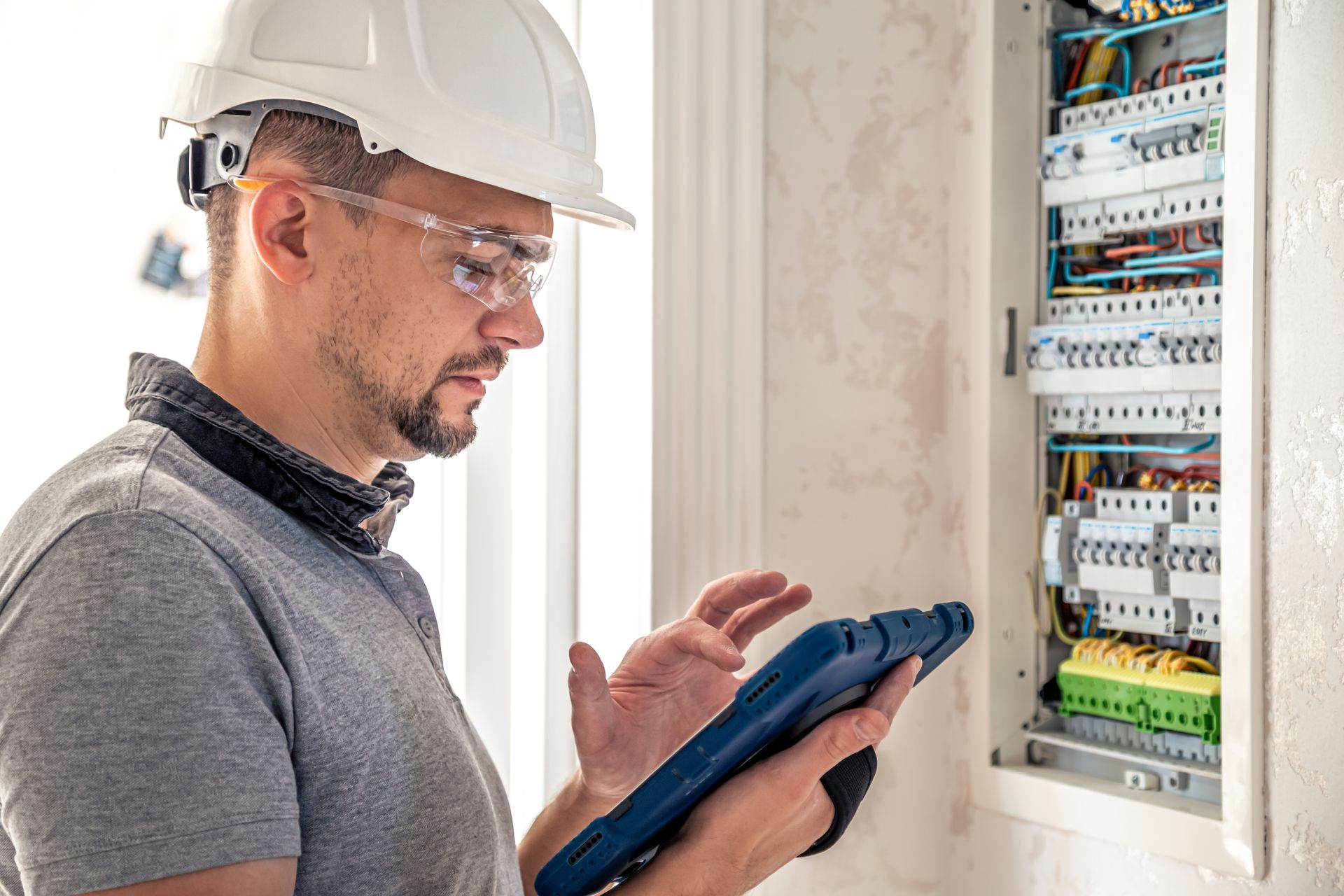 Technician in a hard hat checks an electrical panel with a tablet