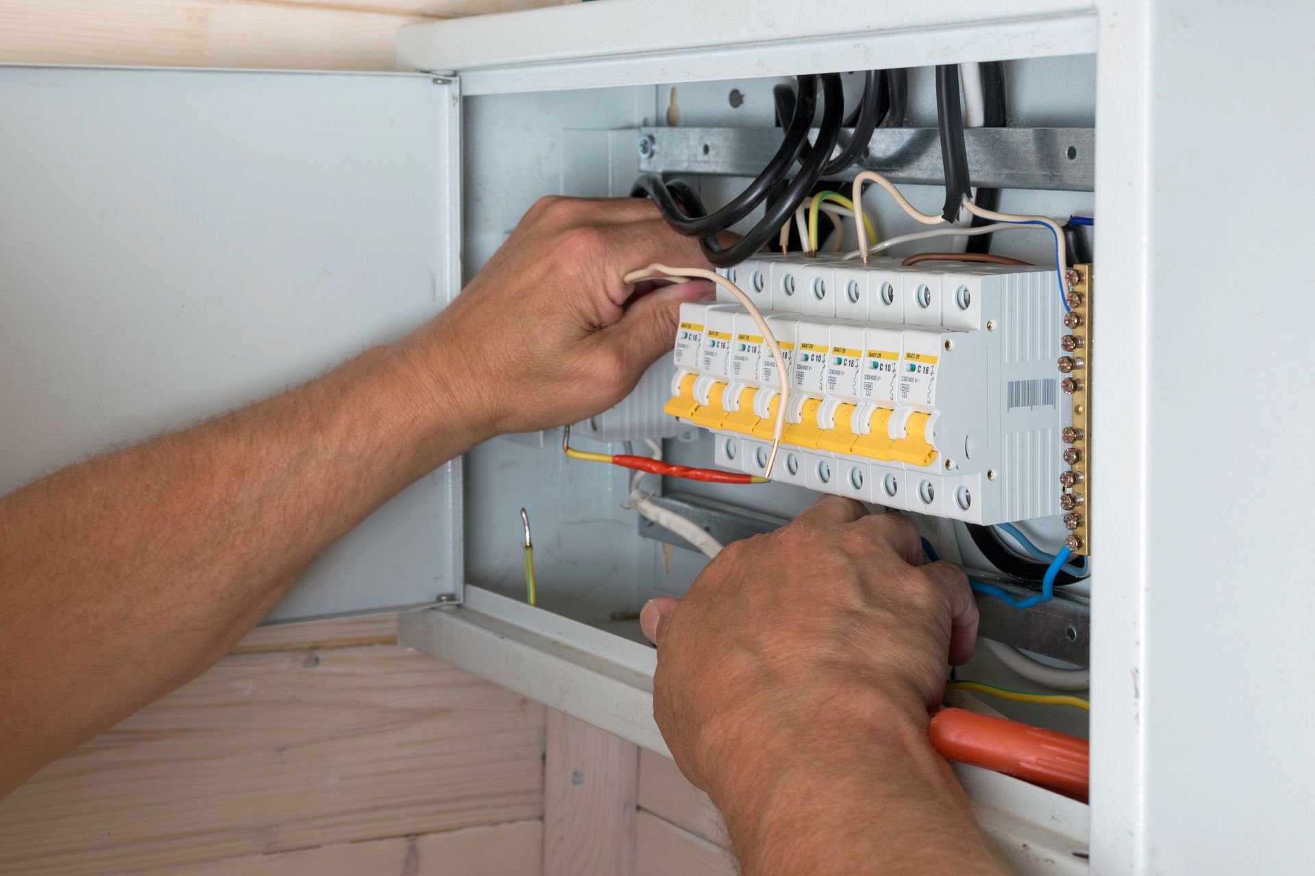 Hands wiring a home electrical breaker panel inside an open cabinet.