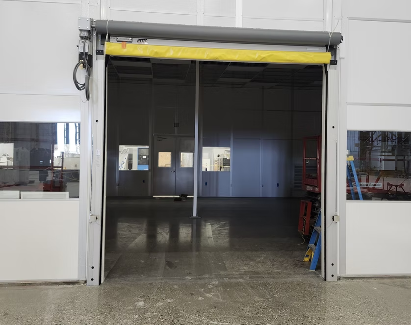 Open industrial doorway with a yellow roll-up door and dim interior visible beyond white walls.