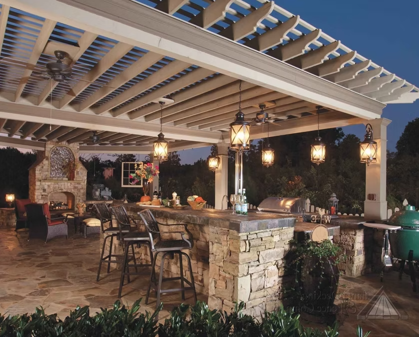 Outdoor stone patio dining area under a pergola with hanging lanterns and empty tables and chairs at dusk