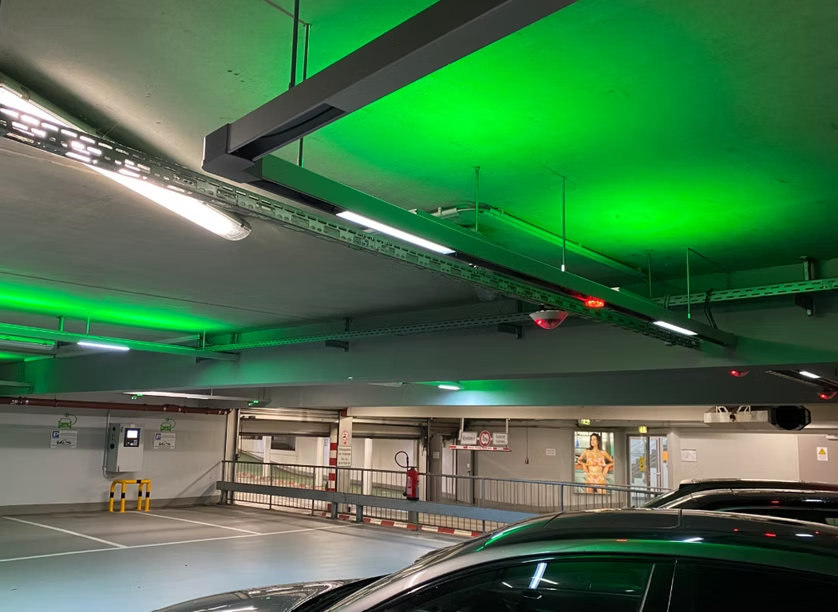 Underground parking garage with green ceiling lights and a black car in the foreground