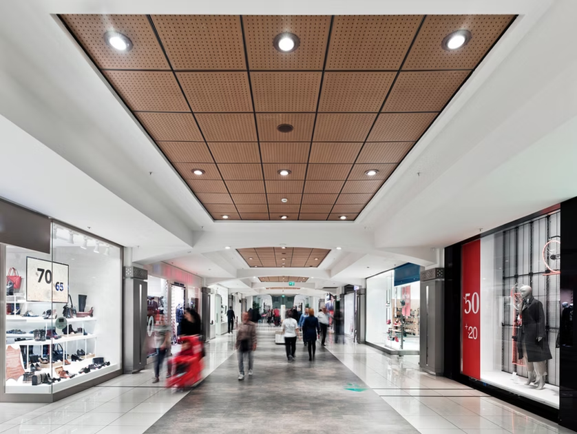 Bright shopping mall corridor with storefronts, sale signs, and a few blurred shoppers walking through.