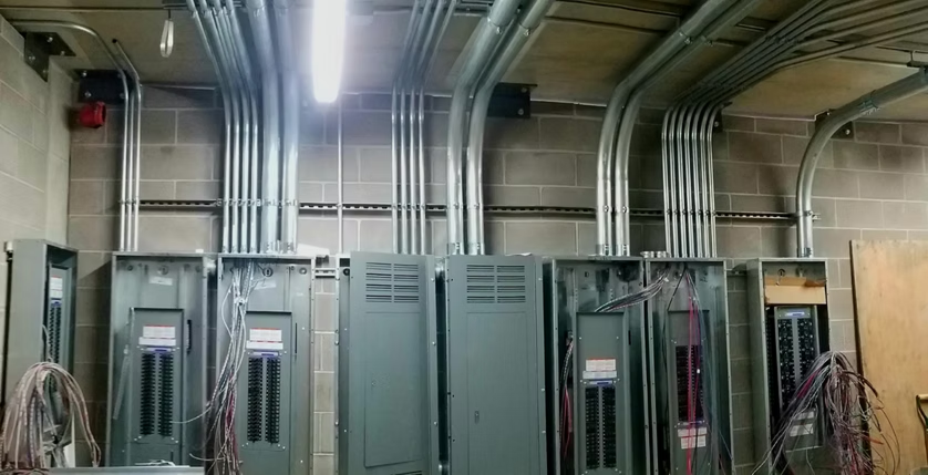 Electrical room with tall gray cabinets, overhead conduit, and coiled cables along the walls