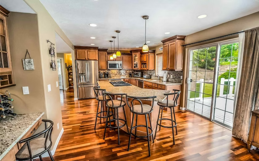 Bright kitchen with island, bar stools, wood floors, and sliding glass doors to a patio.