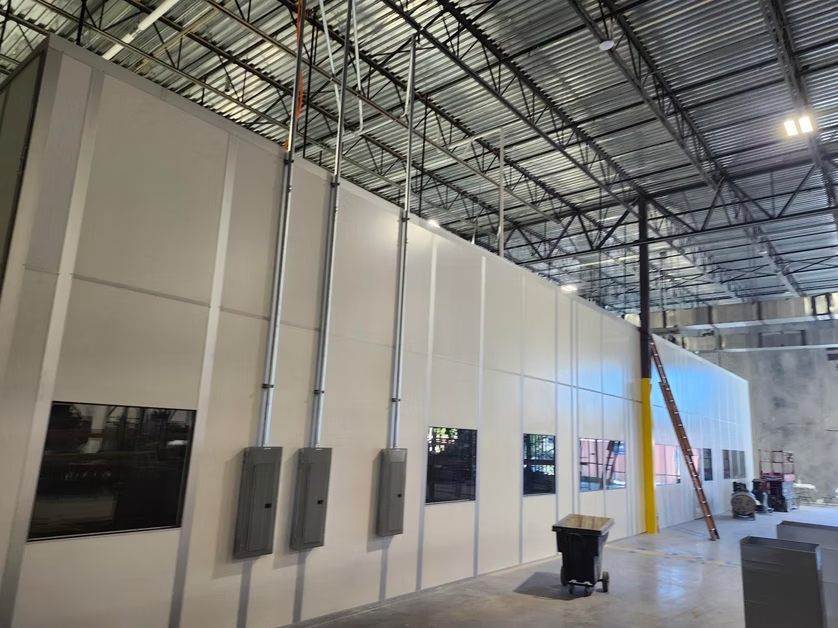 Large industrial warehouse with white wall panels, electrical boxes, and exposed steel roof framing