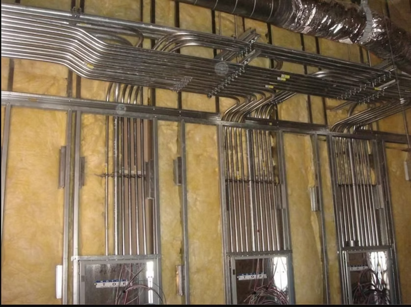 Electrical conduits and ducts on an unfinished wall with exposed insulation.