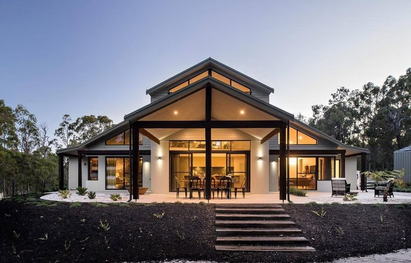Modern house at dusk with warm-lit porch, front steps, and surrounding trees