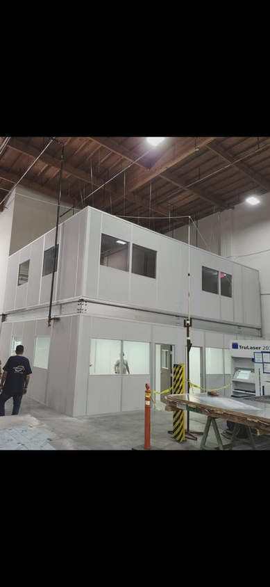 Industrial warehouse interior with a white mezzanine office structure and two workers on the floor