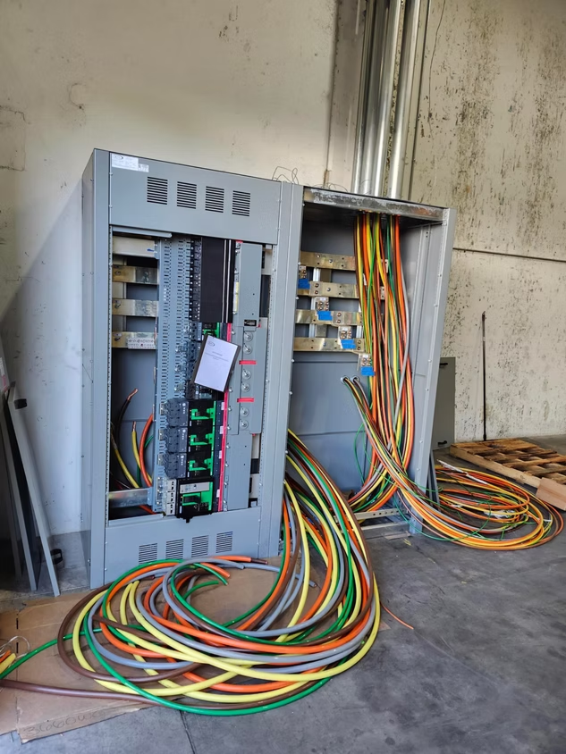 Open electrical control cabinet with colorful cables on a concrete floor in an industrial room