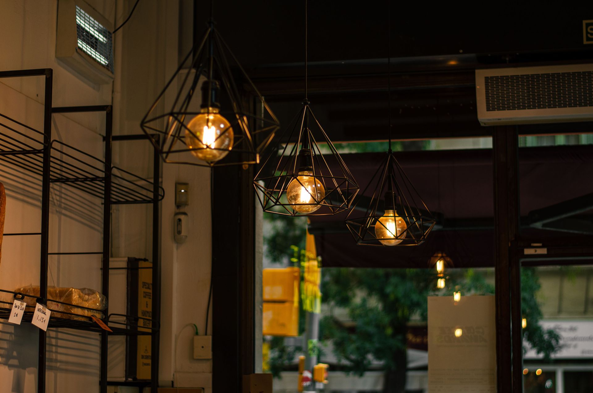 Warm hanging lights inside a cozy café entrance with shelves and street view beyond