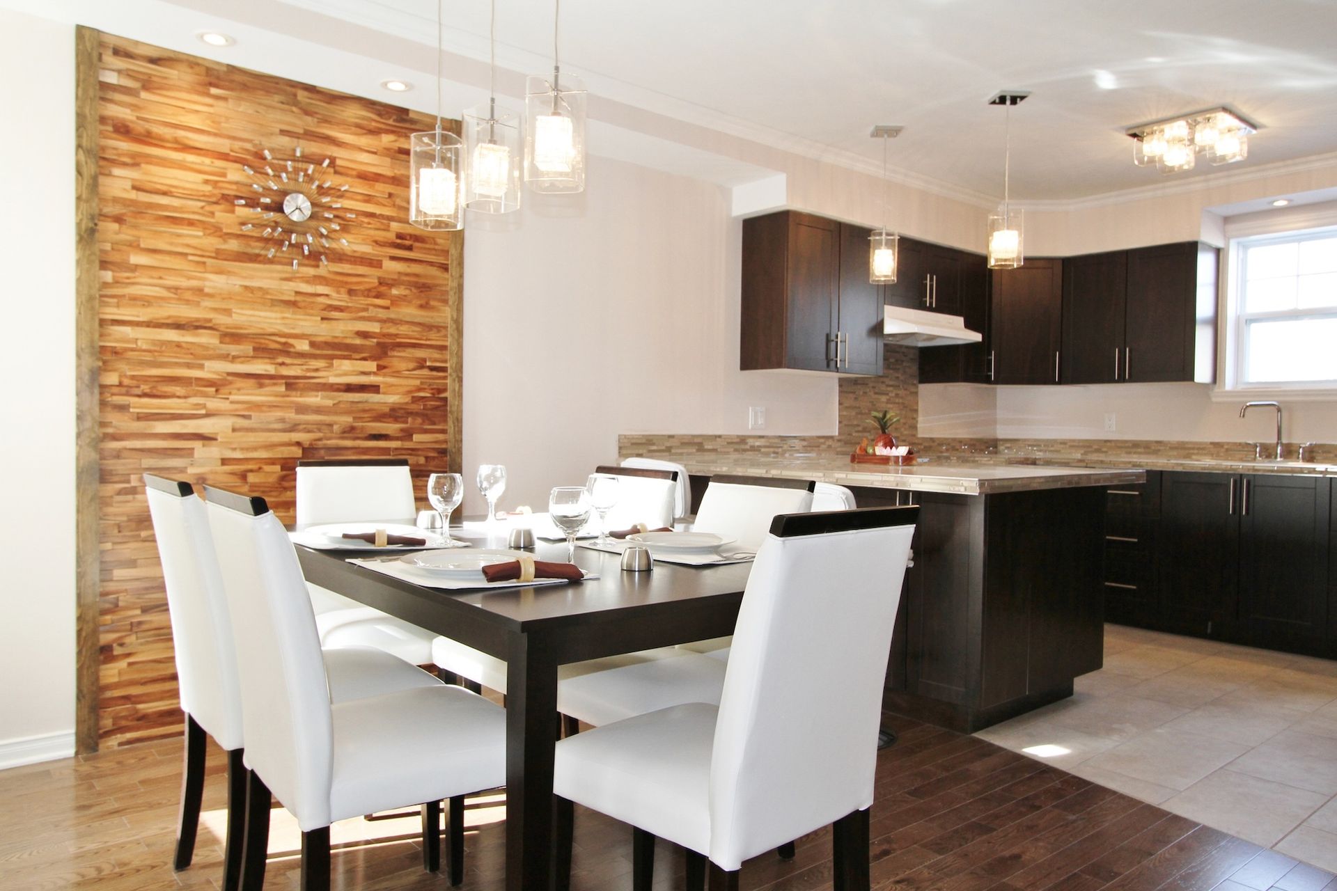 Modern dining and kitchen area with white chairs, dark table, and wood accent wall