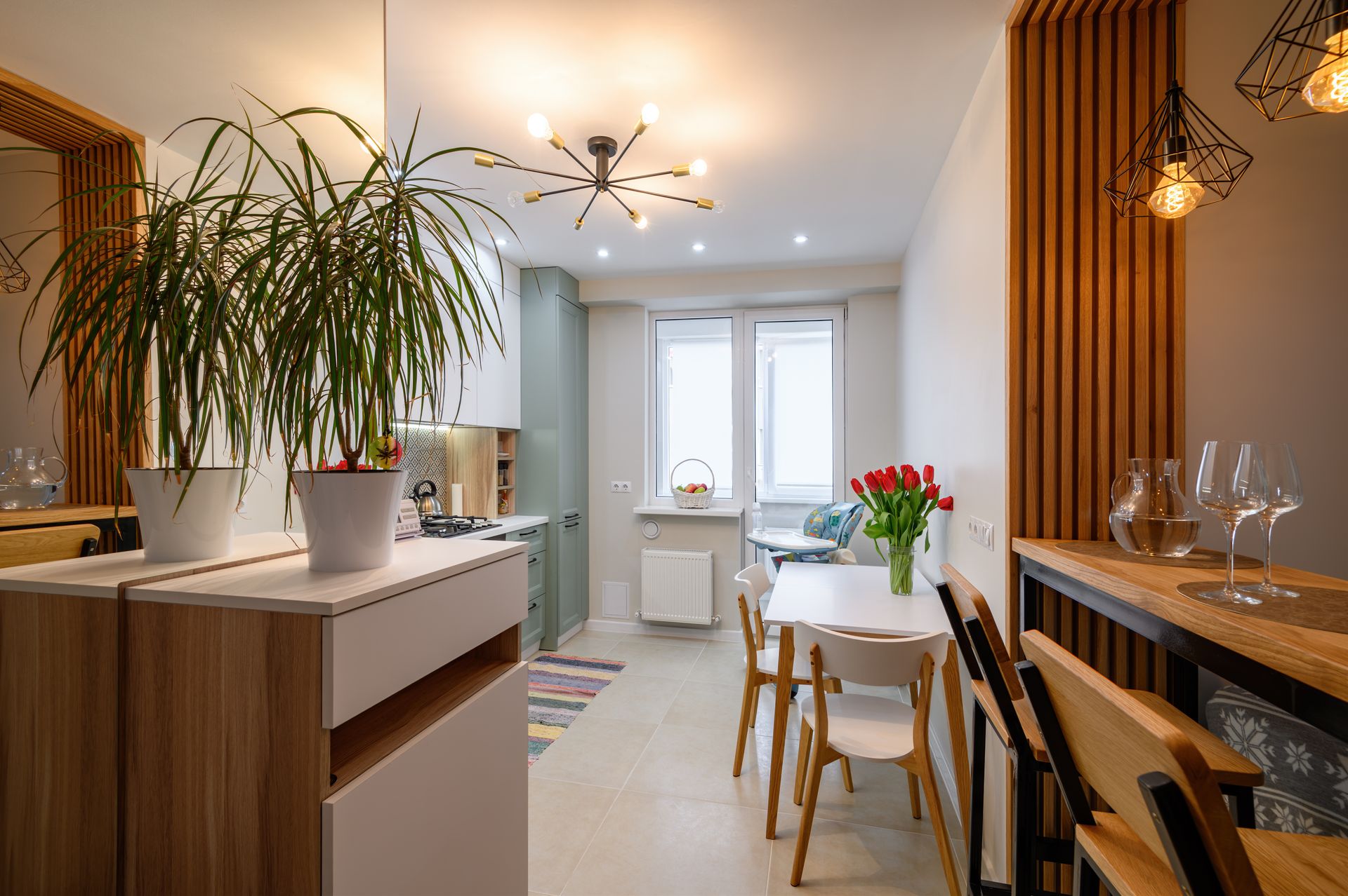 Modern kitchen and dining area with a wooden bar, white table, indoor plants, and bright windows