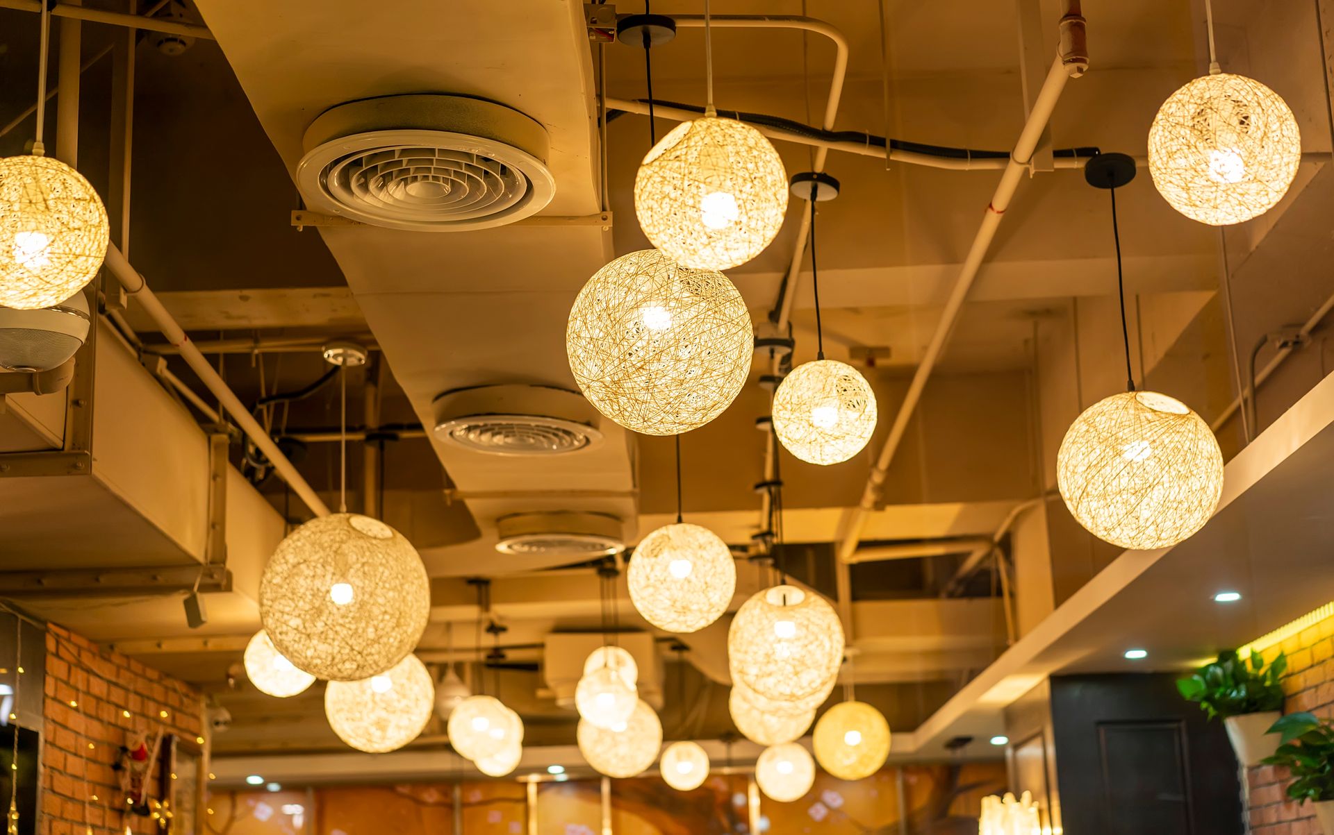 Warm café ceiling with hanging globe pendant lights and exposed ducts