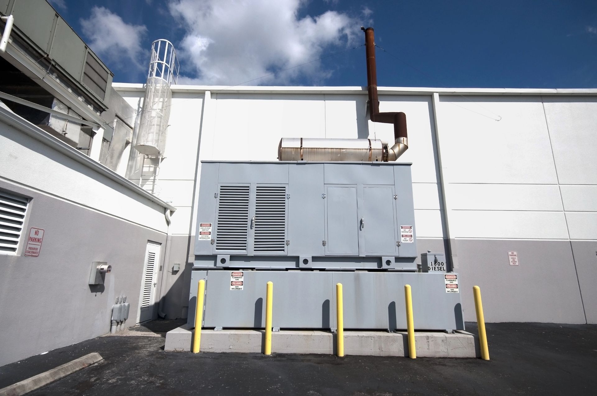 Industrial building exterior with gray HVAC equipment, yellow bollards, and blue sky.