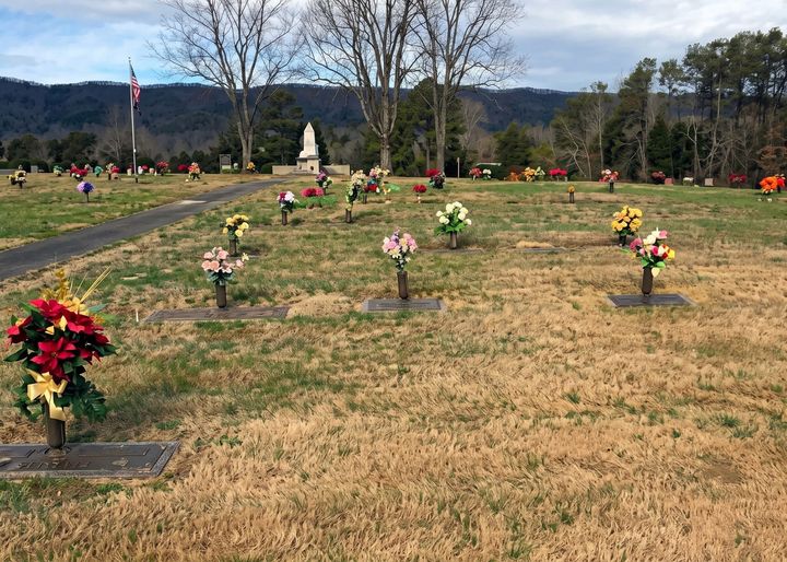 Flower cemetery with colorful bouquets on grave markers in a grassy field, mountains in the background.