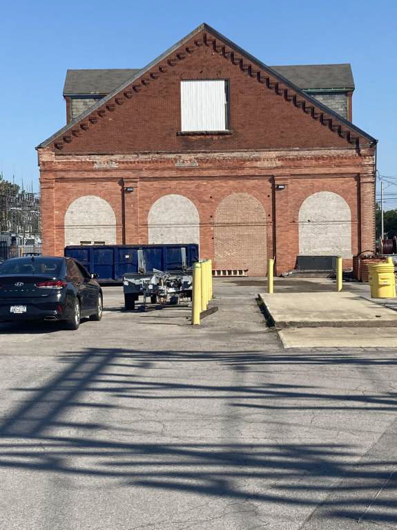 A black car is parked in front of a large brick building.