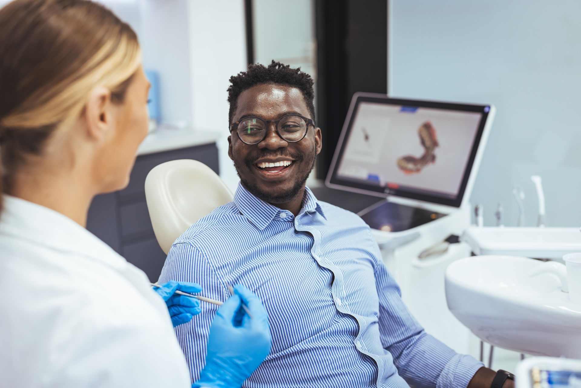 A smiling patient looking at a dentist while being seated in a chair at a dentist's office.