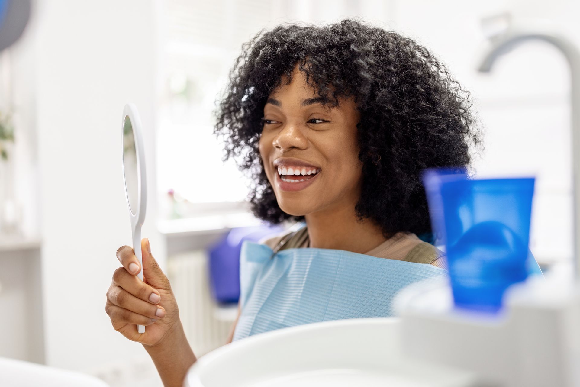Happy patient examining her teeth in a mirror following a successful dental treatment