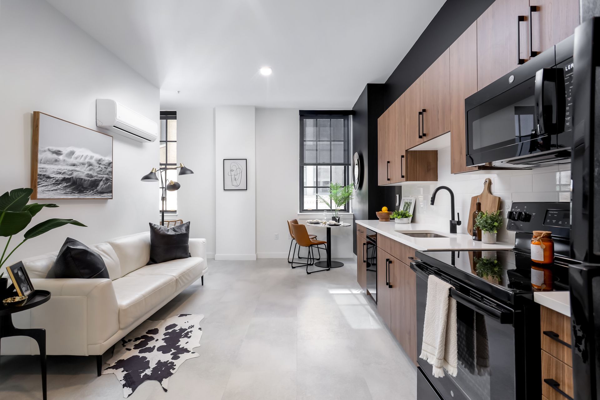 Modern apartment kitchen and living area with light wood cabinets, black appliances, and white sofa.