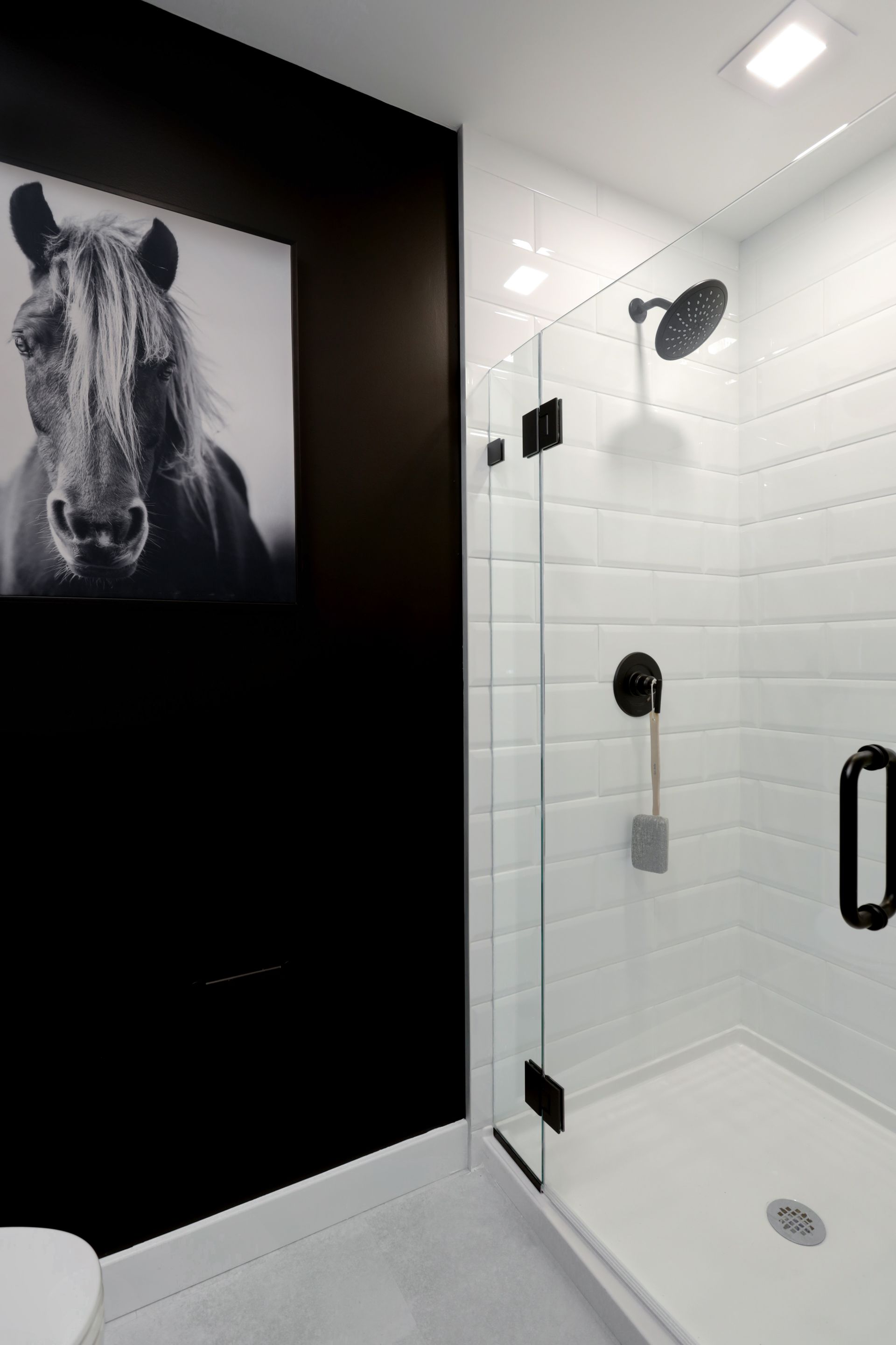 Black and white bathroom with white subway tile, a black horse print, and a glass shower door.