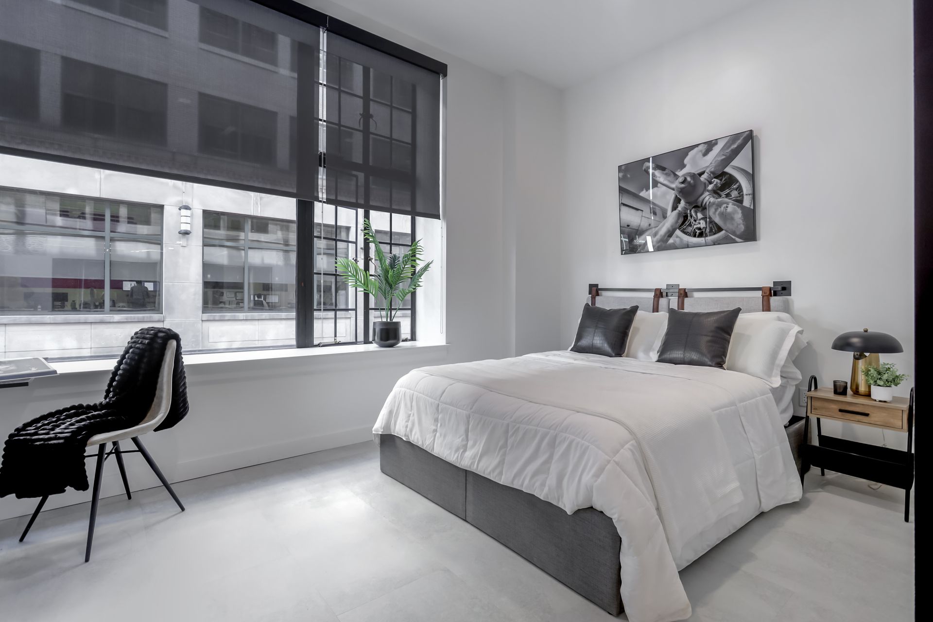 Modern bedroom with white walls, large window, bed, and black and white artwork.